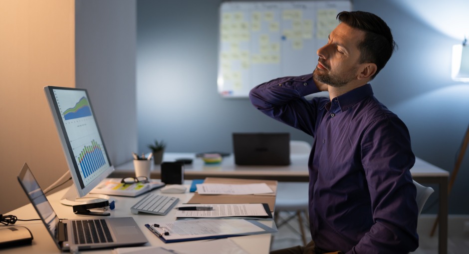 A man with a laptop in front of him trying to stop slouching at his desk. 